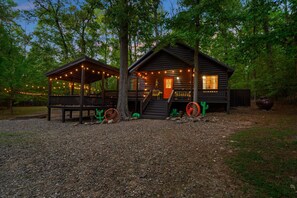 Eine rustikale Holzhütte mit Veranda, einer Treppe zum Eingang und dekorativer Beleuchtung.