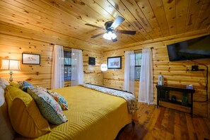 Ein Schlafzimmer einer Holzhütte mit Bett, Deckenventilator, Fernseher und gerahmten Bildern an den Wänden.