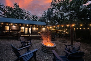 Eine Holzblockhütte mit Feuerstelle, Sitzgelegenheiten im Freien und Lichterketten.