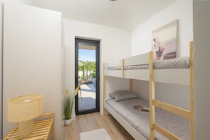Ett rum med en våningssäng, en dörr som leder ut till ett utomhusområde, ett nattduksbord med en lampa och en krukväxt.