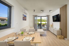 Ett modernt matområde med ett träbord för fyra personer, en soffa, en tv som är monterad på väggen och en skjutdörr i glas som leder ut till en uteplats.