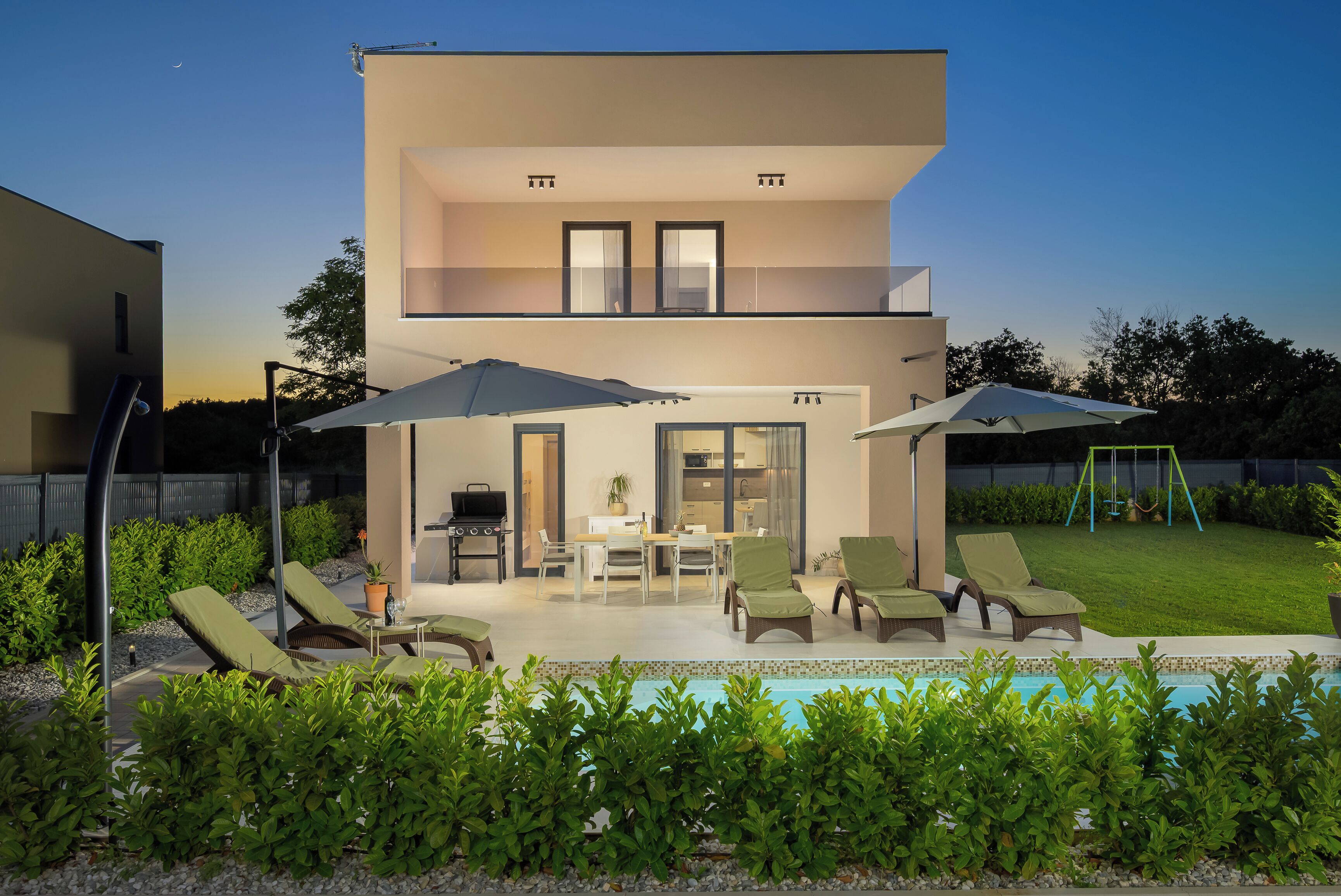 A modern two-story house with a patio, outdoor seating, and a swimming pool.