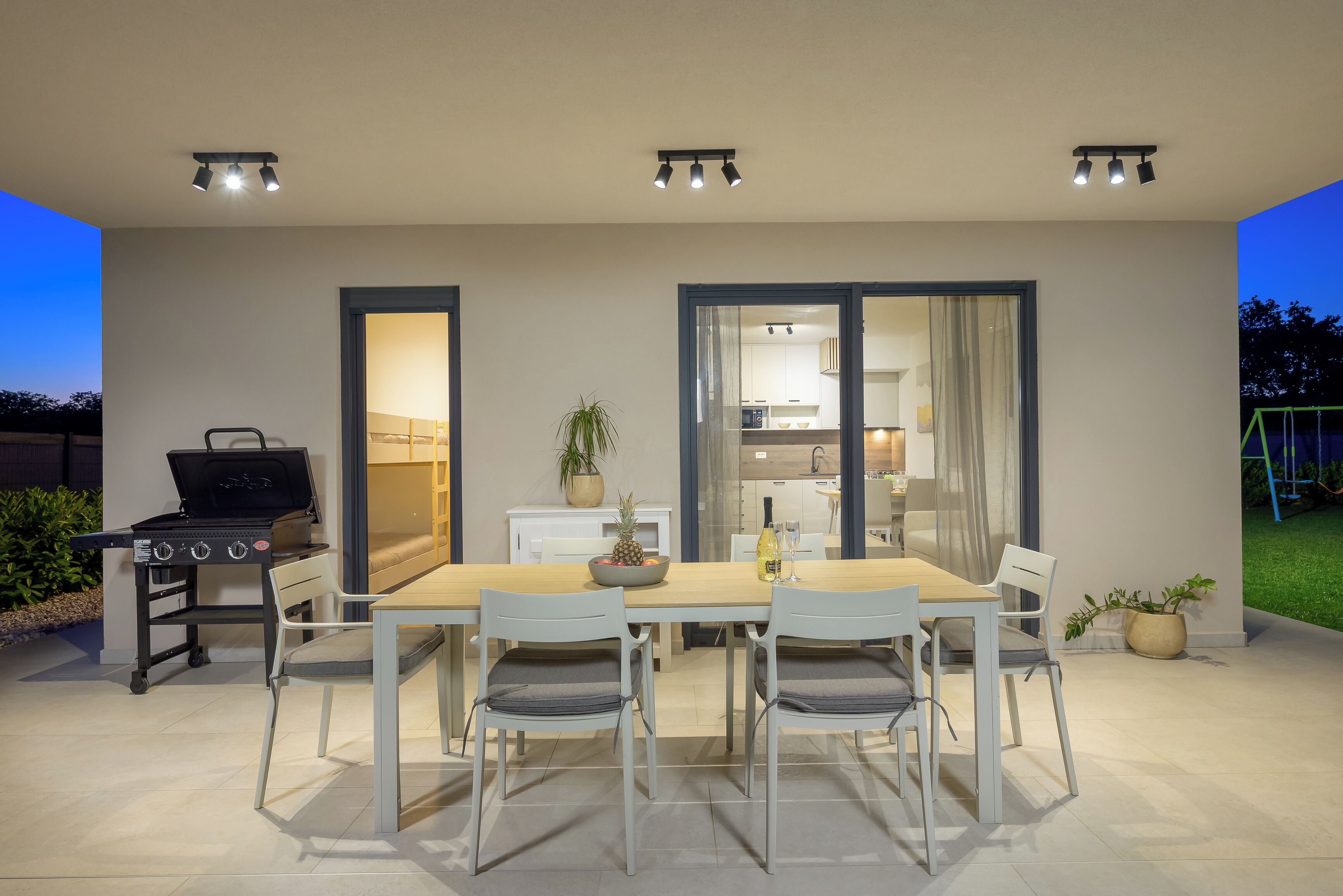 Een terras met eettafel, stoelen, een barbecue en uitzicht op het huis.
