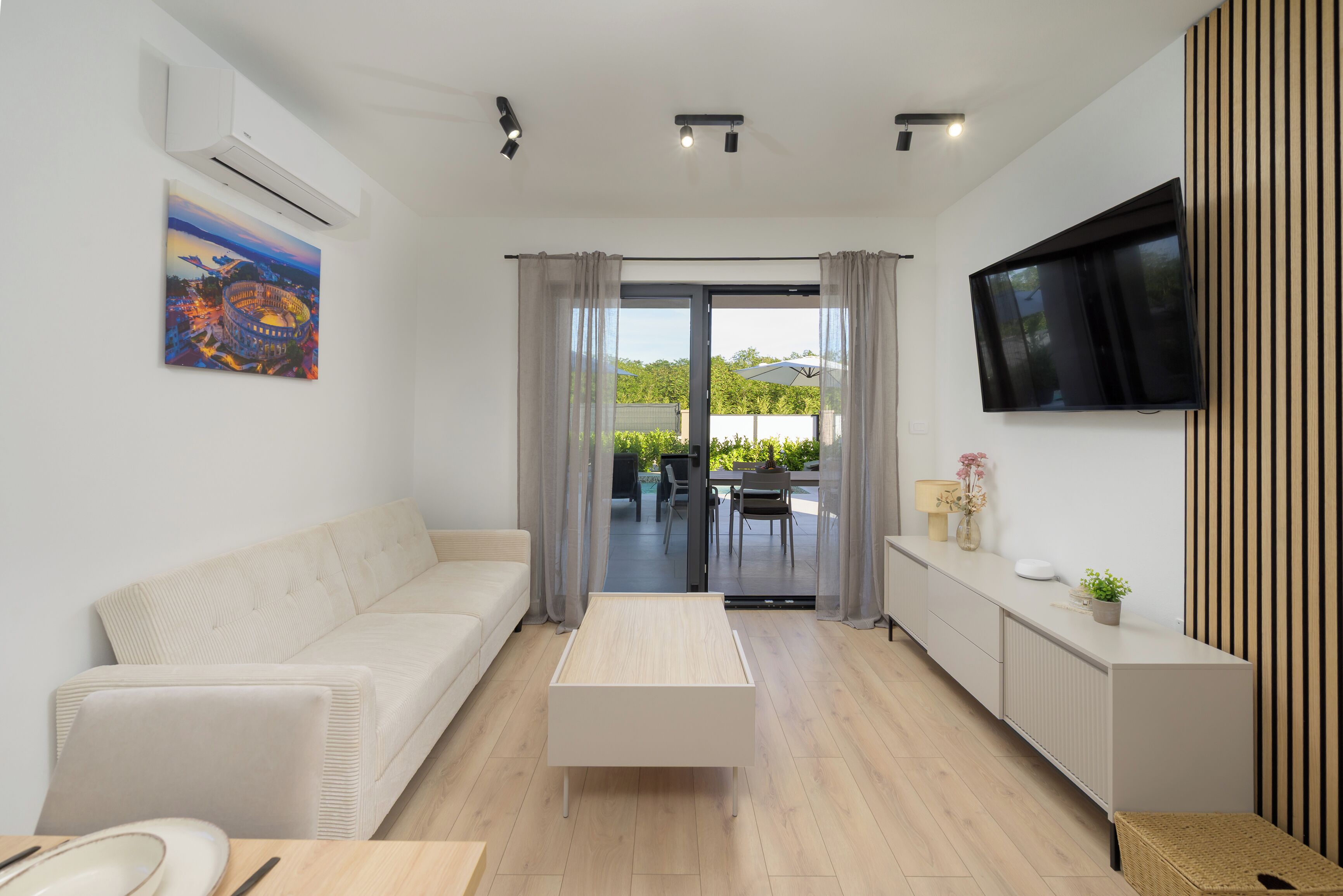 A modern living room with a sofa, a coffee table, a TV, and a sliding glass door leading to an outdoor area.