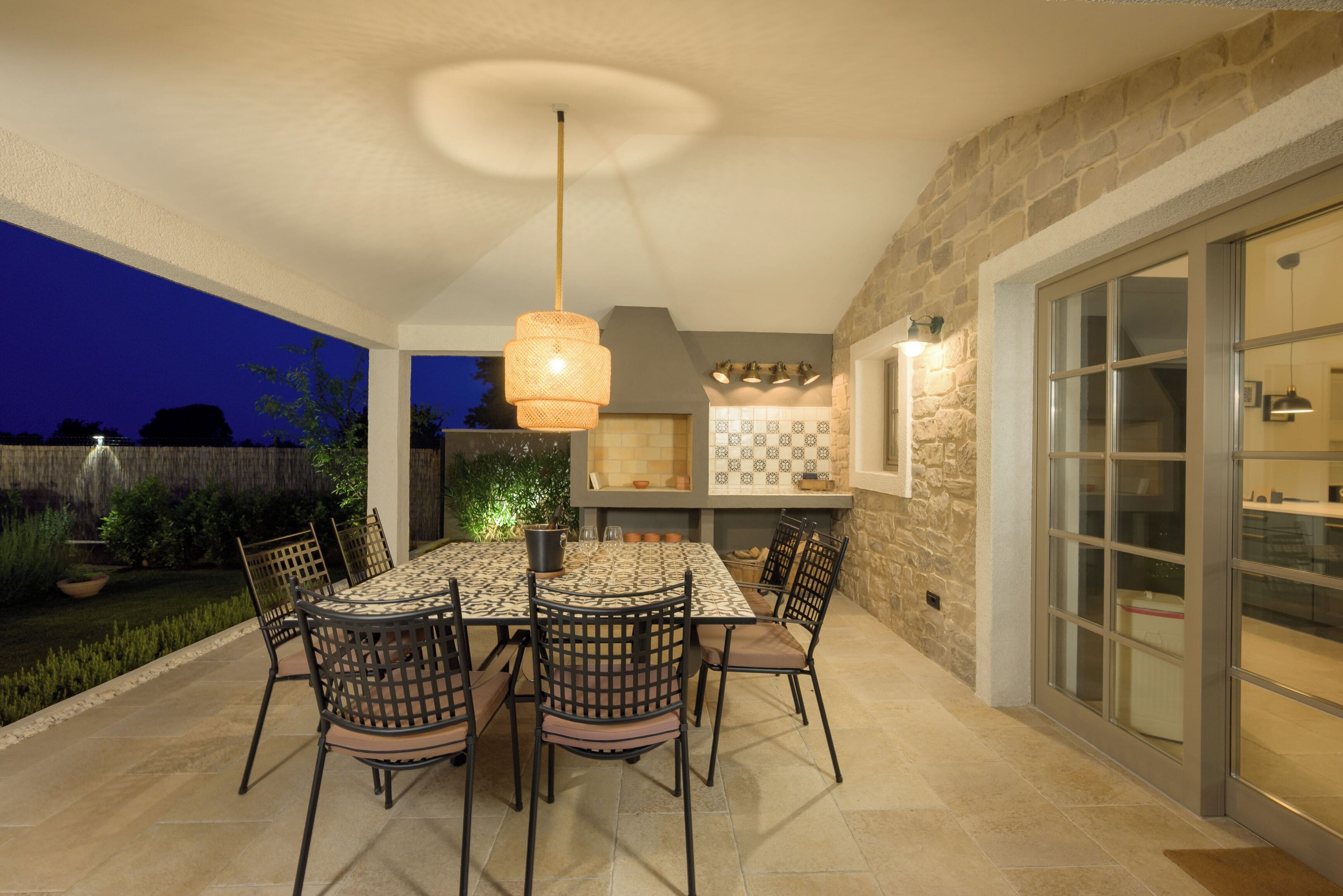 An outdoor patio with a table and chairs, a hanging light fixture, and a stone wall.