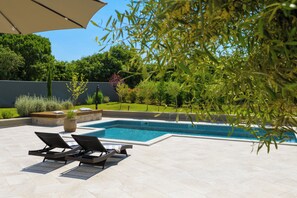 Ein Schwimmbecken mit zwei Liegestühlen und einer überdachten Pergola.