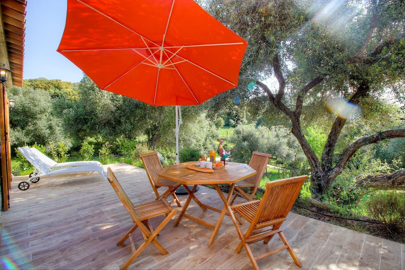 A wooden deck with a table and chairs, a red umbrella, and a lounge chair.