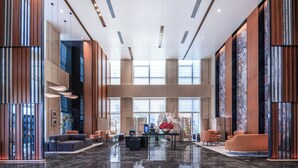 Een ruime lobby met een hoge plafond, grote ramen en moderne inrichting.