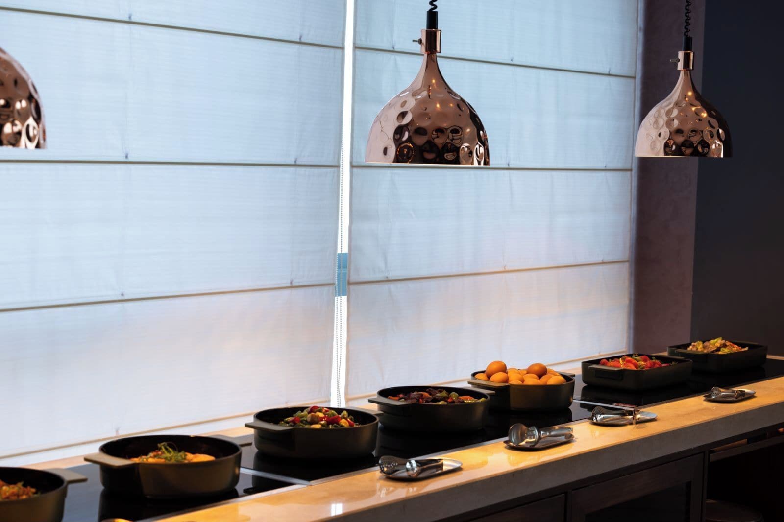 A kitchen counter with multiple cooking stations, each with a pot and a pan, and overhead pendant lights.