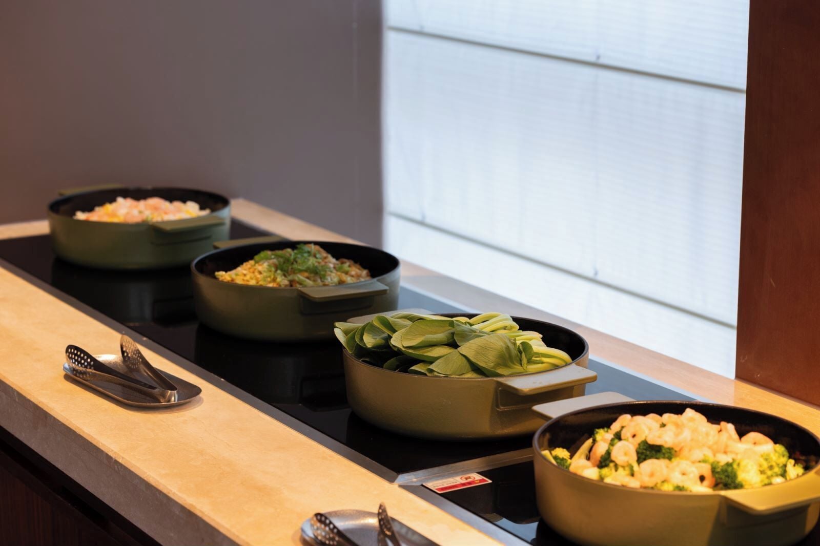 A buffet setup with various dishes in bowls, a spatula, and a spoon on a countertop.