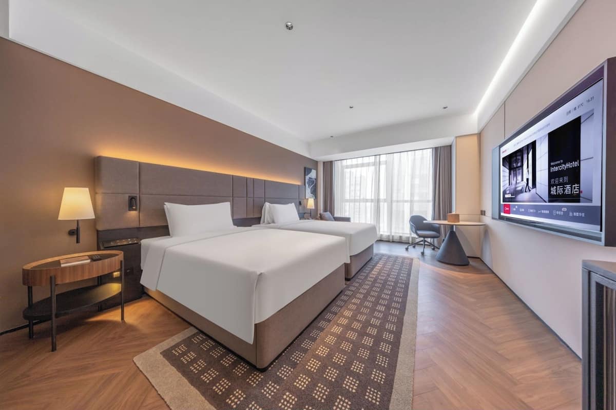Habitación de hotel con una cama grande, mesitas de noche, televisión y vistas a la ciudad.