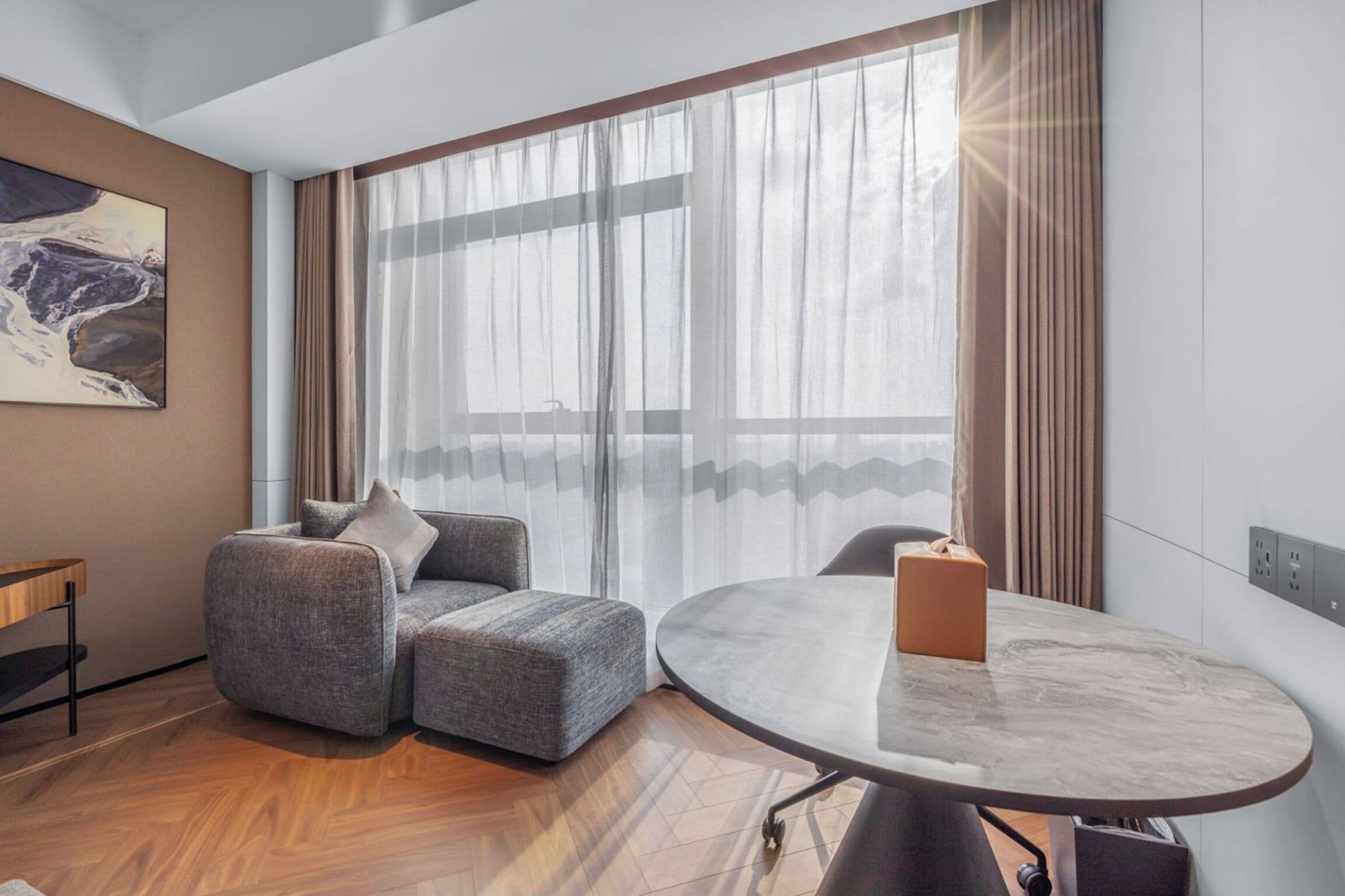 Una habitación moderna con un sofá gris, una mesa redonda y un ventanal con cortinas de gasa.