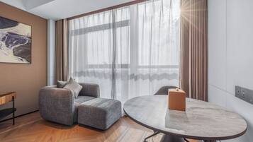 Una habitación moderna con un sofá gris, una mesa redonda y un ventanal con cortinas de gasa.