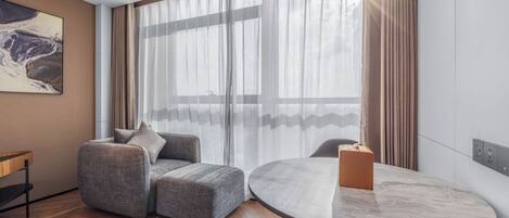 A modern room with a grey sofa, a round table, and a large window with sheer curtains.