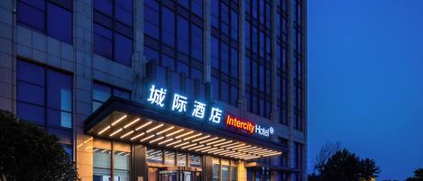 A modern hotel building with illuminated signage, a glass facade, and a well-lit entrance.