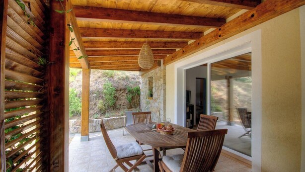 Une terrasse extérieure avec une table et des chaises en bois, un luminaire suspendu et une vue sur le paysage environnant.