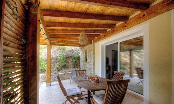 An outdoor patio with a wooden table and chairs, a hanging light fixture, and a view of the surrounding landscape. - Monti - CATERI - Gîte (CATERI)