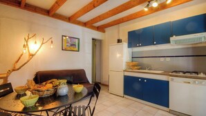 Une cuisine compacte avec des meubles bleus, un réfrigérateur blanc et un coin repas avec une table dressée pour deux personnes.