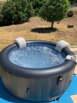 Ein aufblasbarer Whirlpool mit Pumpe, umgeben von einer blauen Matte, draußen mit Baum und trockenem Gras im Hintergrund.