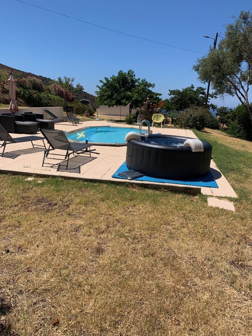 A backyard with a swimming pool, lounge chairs, a hot tub, and a grassy lawn.