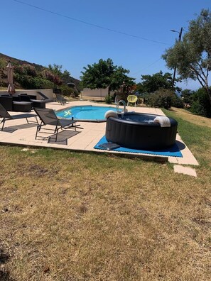 Ein Garten mit Swimmingpool, Liegestühlen, Whirlpool und Rasenfläche.