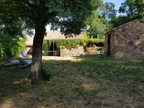 Ein Steinhaus mit Ziegeldach, ein Baum im Vordergrund und Außenbestuhlung.