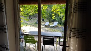 A patio area with a table and chairs, a view of a garden with trees and a lawn, and a wooden ceiling. - Gîte U Forro - SARI SOLENZARA (SARI SOLENZARA)
