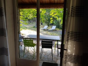 Eine Terrasse mit Tisch und Stühlen, Blick auf einen Garten mit Bäumen und einer Rasenfläche, sowie eine Holzbalkendecke.