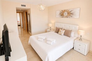 A hotel room with a large bed, two bedside tables, a TV, a chandelier, and a wall art piece. - Stylish Sea-View Retreat in Casares Playa (Casares)