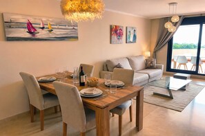 A dining area with a wooden table, chairs, and a painting of sailboats. - Stylish Sea-View Retreat in Casares Playa (Casares)