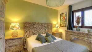 Ein Schlafzimmer mit einem großen Bett, zwei Nachttischen, einem dekorativen Kopfteil, einem Fenster mit Vorhängen und einem Wandbild.