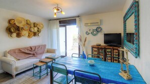 Ein Zimmer mit einem weißen Sofa, einem blauen Tisch, einem Fernseher und einer Wand mit Hüten.