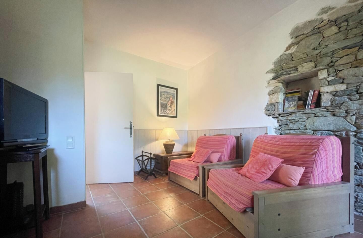 Una habitación con dos camas, televisión, lámpara y una pared de piedra.