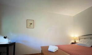 A bedroom with a bed, a nightstand with a lamp, a small table with a lamp, and a framed picture on the wall.
