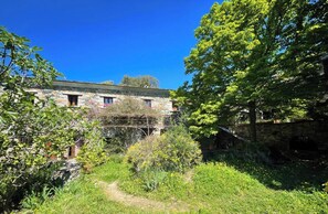 A stone building with multiple windows and a garden area with various plants and a path.