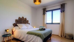 A bedroom with a bed, bedside lamp, window with curtains, and a wall-mounted light fixture. - Le grand gîte d'Elodie (TALLONE)