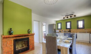 Ein Essbereich mit Kamin aus Ziegelsteinen, einem für vier Personen gedeckten Tisch und einer Küche im Hintergrund.