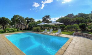 Piscina retangular com borda azulejada, rodeada por um muro de pedra e um terraço pavimentado.