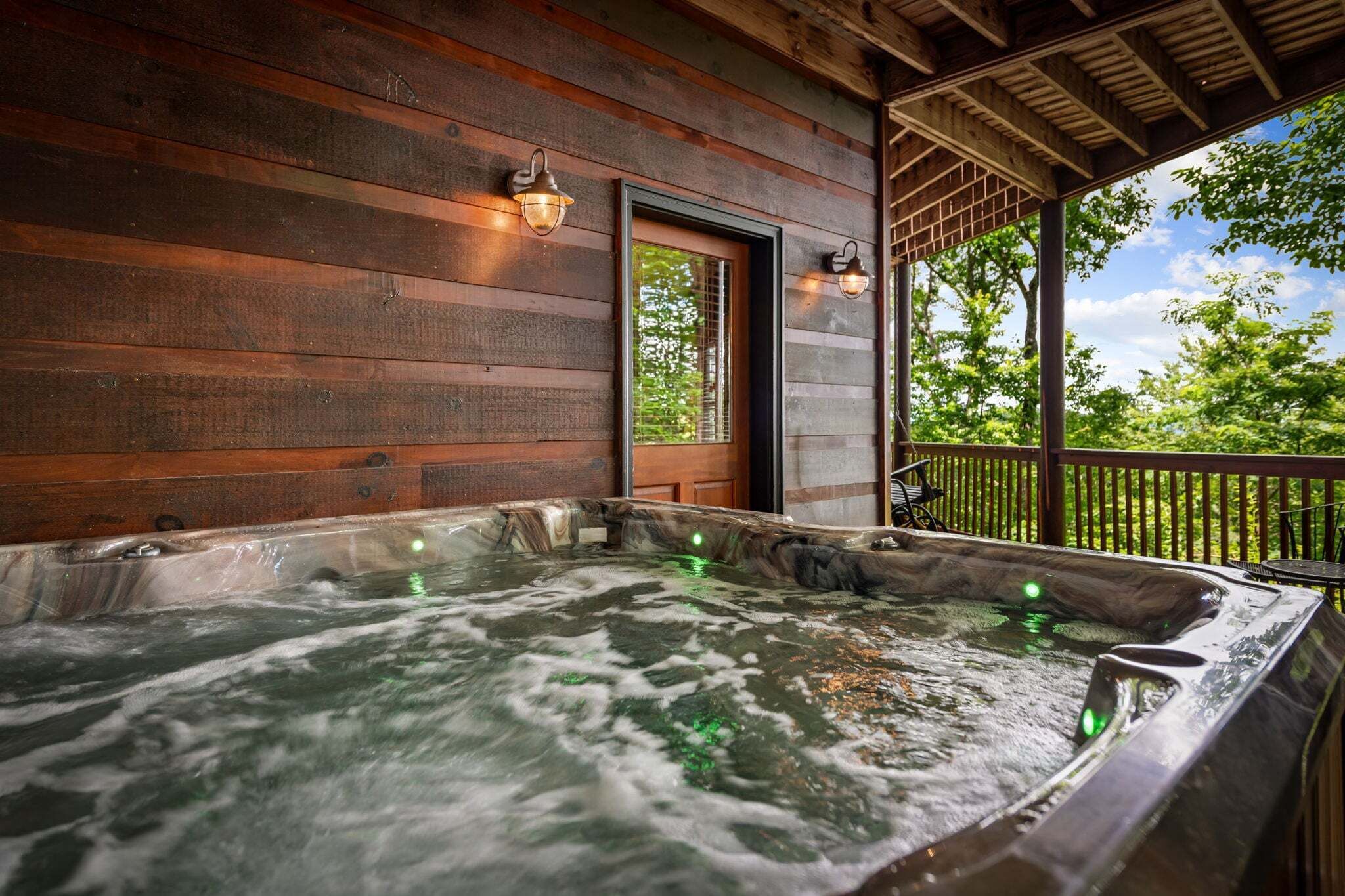 A wooden cabin with a hot tub and a balcony with a view of trees.