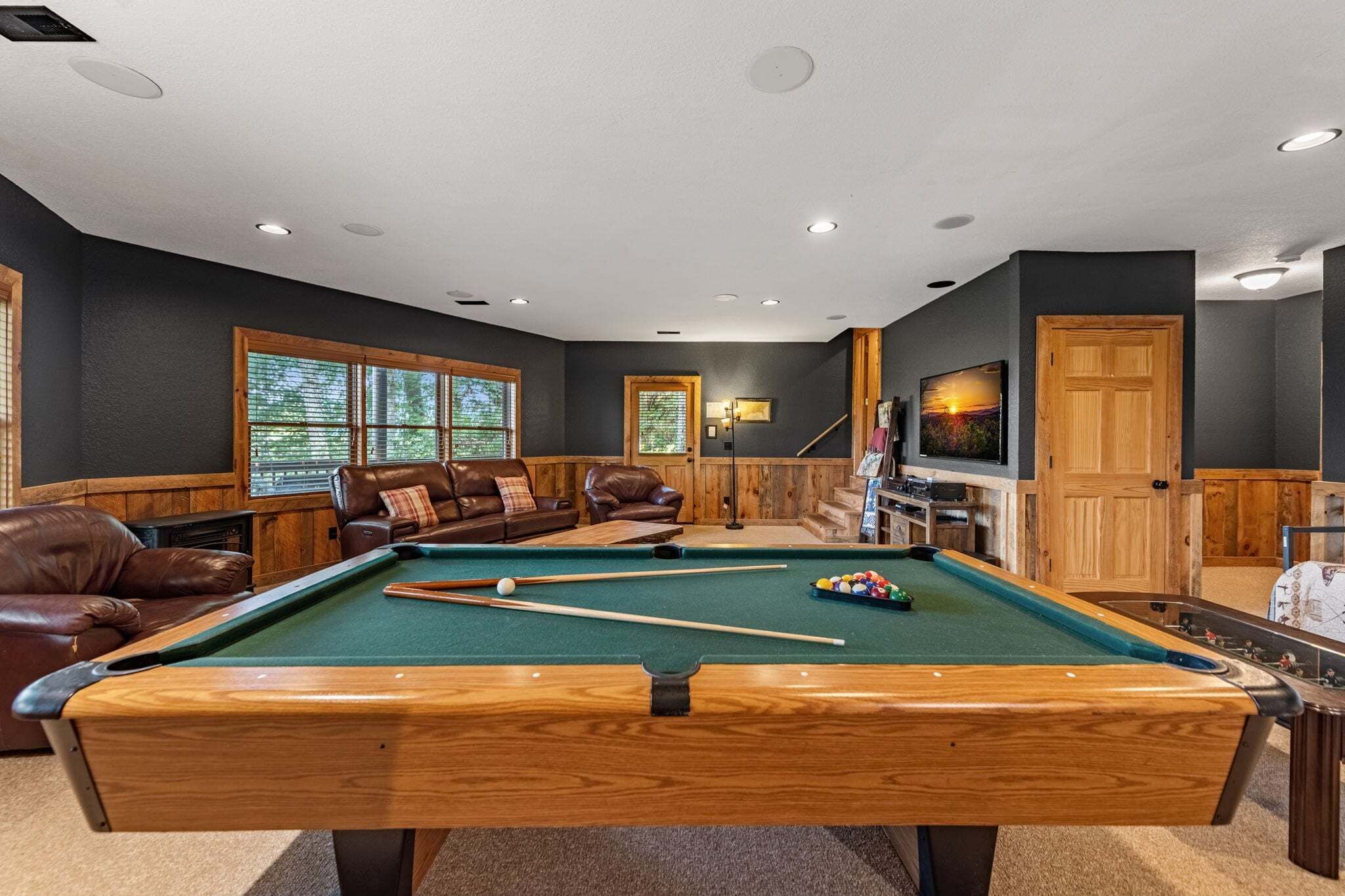 A pool table with a green felt surface, surrounded by leather sofas and a television.