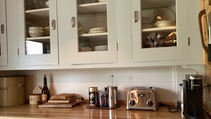 A kitchen with white cabinets, a wooden countertop, a bread maker, a toaster, a coffee maker, and salt and pepper shakers.