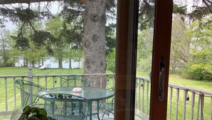 A covered outdoor area with a table and chairs, a wooden deck, and a view of a grassy area with trees.