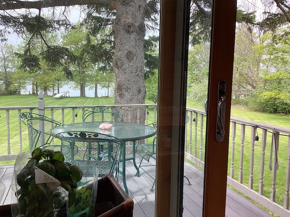A covered outdoor area with a table and chairs, a wooden deck, and a view of a grassy area with trees.