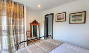 Ein Schlafzimmer mit einem Bett, einem Holzstuhl, einem Spiegel und zwei gerahmten Bildern an der Wand.