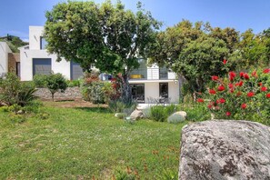 Ein modernes Haus mit Garten, einem großen Felsen und einem Baum.