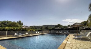 Ein Schwimmbecken mit Liegestühlen und Sonnenschirmen, umgeben von einer Hecke und Grünpflanzen.
