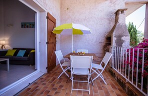 Eine Terrasse im Freien mit Tisch und Stühlen, einem gelb-weißen Sonnenschirm und einer Ziegelwand.