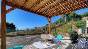 An outdoor patio with a wooden pergola, white chairs, a table with food, and a view of a hillside. - Le 62861 - FARINOLE - Gîte (FARINOLE)