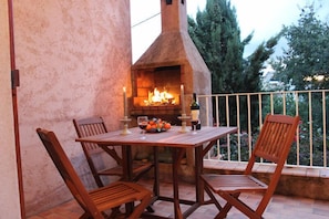 Eine Terrass mit Backsteintisch, Holzsesseln, einem Backofen und einem Geländer.