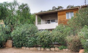 Ein zweistöckiges Haus mit Balkon, umgeben von dichter Vegetation und einem Schotterweg.